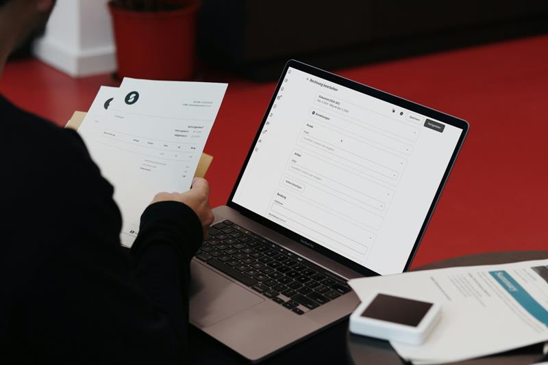 Paper invoices next to a laptop showing a data entry form