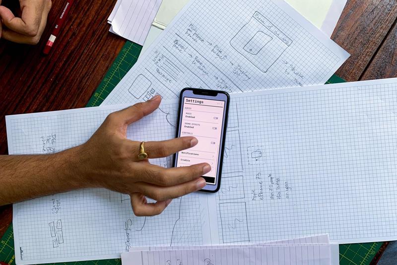 Hand holding a smartphone over paper sketches of app screens